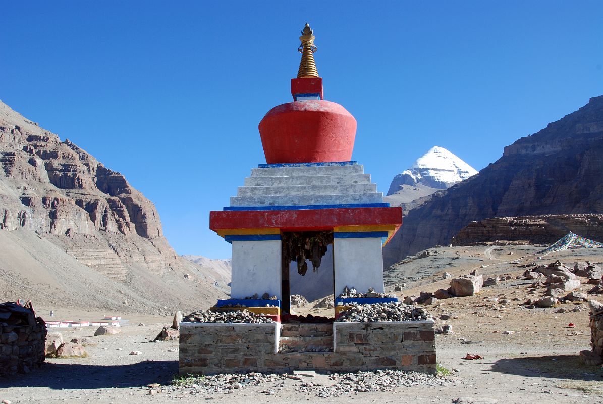 07 Kangnyi Chorten With Mount Kailash Behind On Mount Kailash Outer Kora Just to the west of Tarboche is Kangnyi Chorten (08:38), meaning two-legged chorten, with Mount Kailash behind and Tarboche to the right. It is auspicious act for a pilgrim to walk through the small chorten archway.